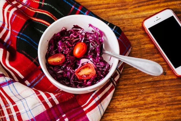 Elevated view of fresh tomatoes and red cabbage in bowl near smartphone