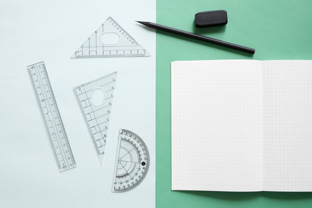 Elevated view of geometric equipment; notebook; pencil and eraser on dual colorful background