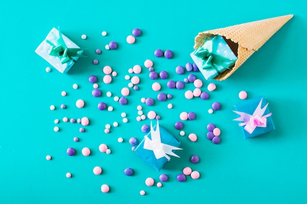 Elevated view of gift boxes; candies and waffle ice cream cone on green background