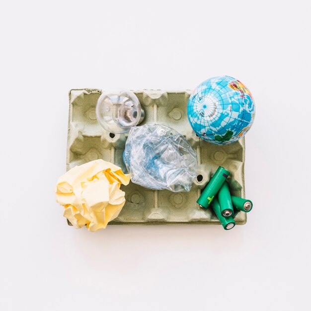 Elevated view of globe, light bulb, crumpled paper, plastic bottle and batteries on egg carton