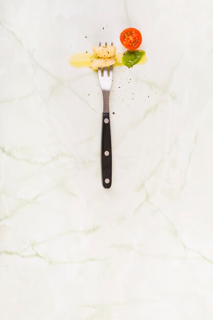 Elevated view of gnocchi pasta with fork near cherry tomato and basil leaf