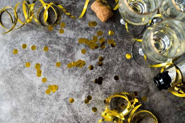 Elevated view of golden confetti and streamers with empty glass over concrete textured