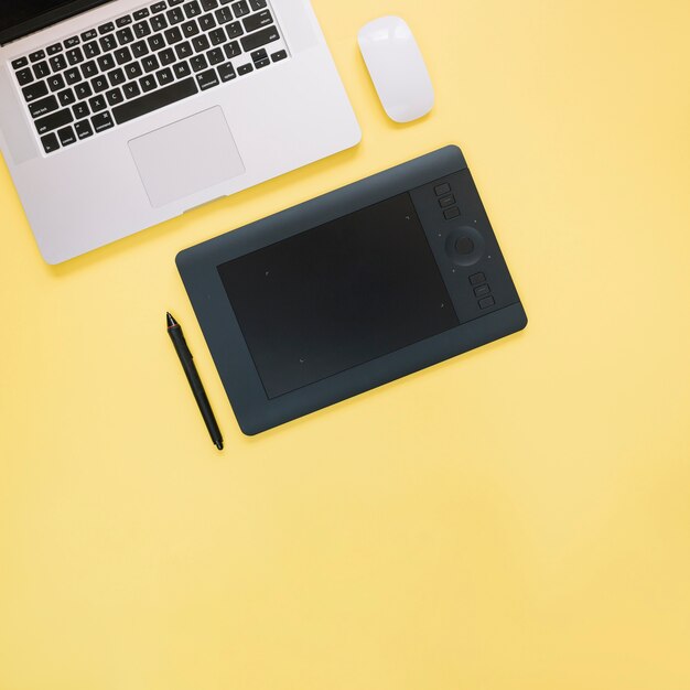 Elevated view of graphic digital tablet and laptop on yellow background