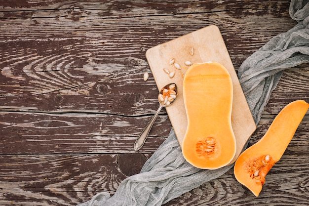 Free photo an elevated view of halved butternut squash with seeds on chopping board over the wooden desk