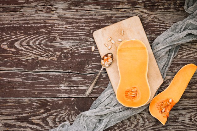 An elevated view of halved butternut squash with seeds on chopping board over the wooden desk