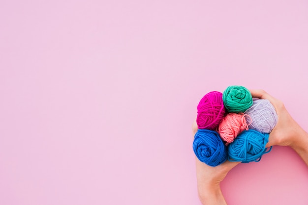 Free photo an elevated view of hand holding colorful wool on pink background