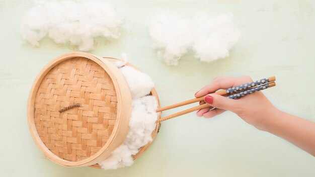 Elevated view of a hand holding cotton with chopsticks from wicker steamer