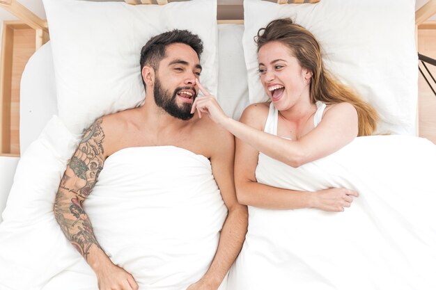 Повышенный вид счастливой женщины, касаясь носа своего друга на кровати