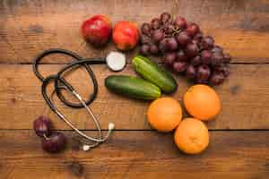 Free photo elevated view of healthy fruits with stethoscope on wooden background