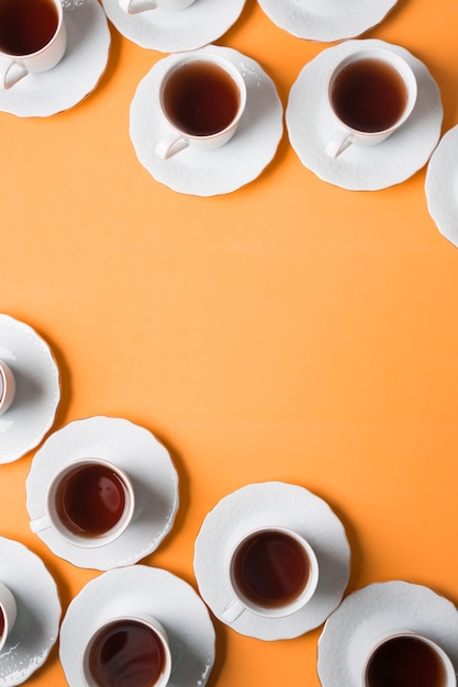 An elevated view of herbal tea cup and saucers on the corner of an orange background