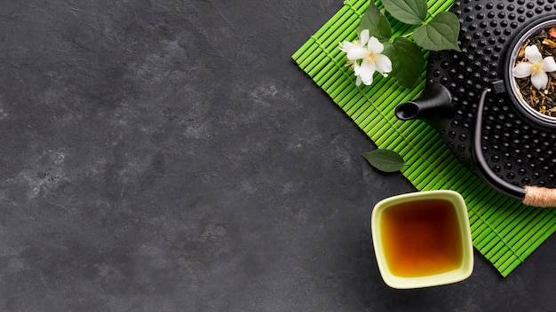 Повышенный вид травяного чая и его ингредиента на черной текстурированной поверхности