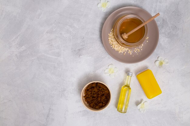 An elevated view of honey; yellow soap; essential oil bottle; coffee powder with white flowers on concrete backdrop