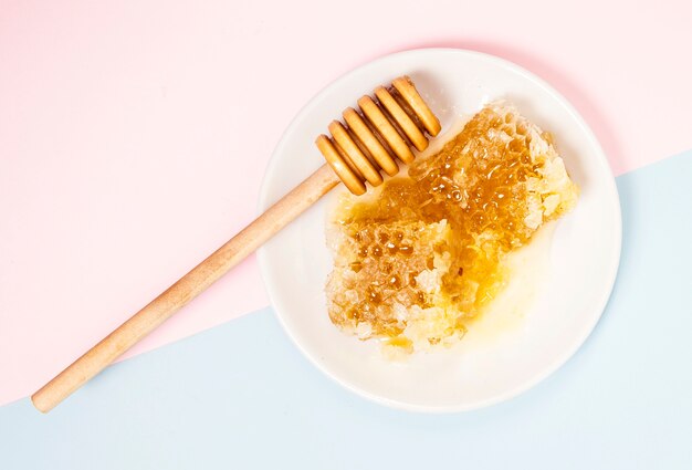 elevated view of honeycomb and wooden honey dipper in white plate