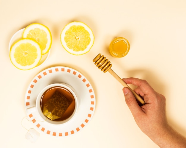 健康茶とレモンスライスに近い蜂蜜ディッパーを持っている人間の手の立面図