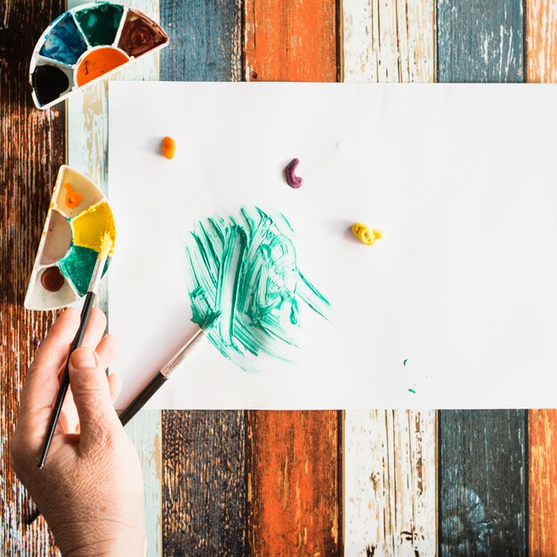 Elevated view of human hand painting on white sheet on grunge wooden background