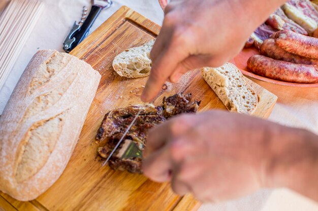 Elevated view of a human hand slicing cooked meat on wooden chopping board