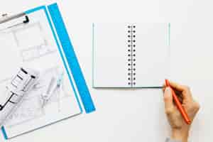 Free photo elevated view of human hand writing on diary near blueprint clipboard