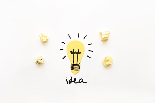 Free photo elevated view of illuminated light bulb with idea word and crumpled paper