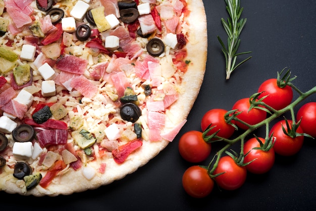 Elevated view of italian fresh pizza and ingredient on black surface