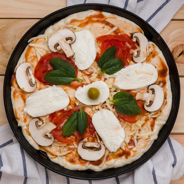 An elevated view of italian pizza with cheese; basil; tomatoes and olives on wooden table