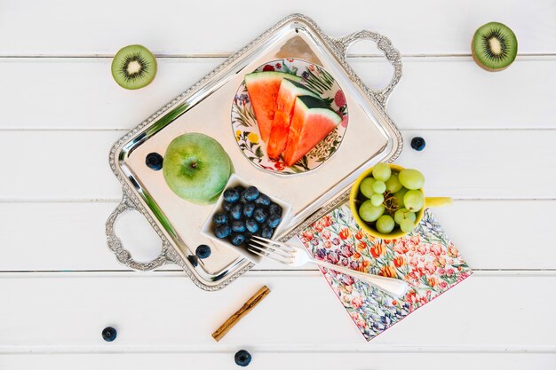 Elevated view of kiwi and grapes near blueberries; sliced watermelon and apple on tray