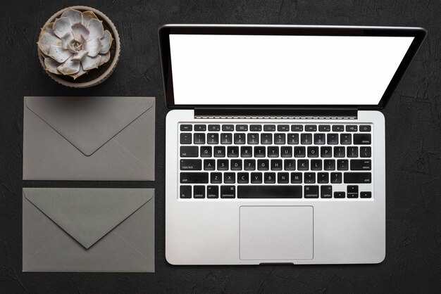 Elevated view of laptop; envelope and succulent plant on black surface