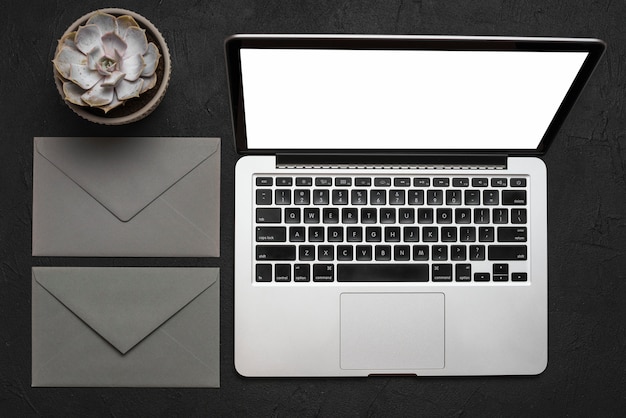 Elevated view of laptop; envelope and succulent plant on black surface