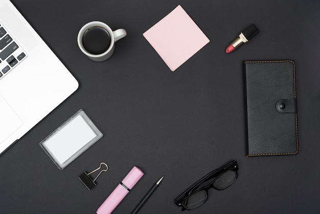 Elevated view of laptop; lipstick; coffee cup and office stationery over black backdrop