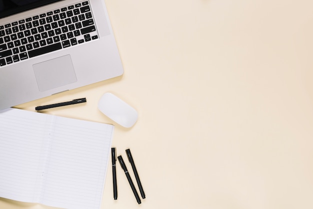 Elevated view of laptop and notebook on cream background