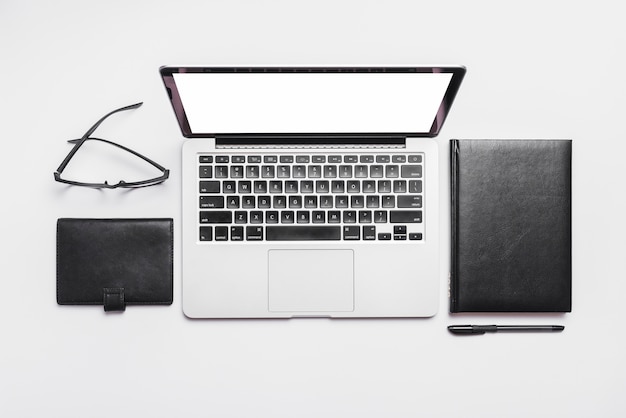 Elevated view of laptop; spectacles and diaries on white background