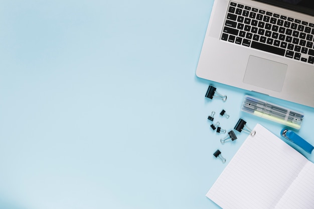 Free photo elevated view of laptop and stationeries on blue backdrop