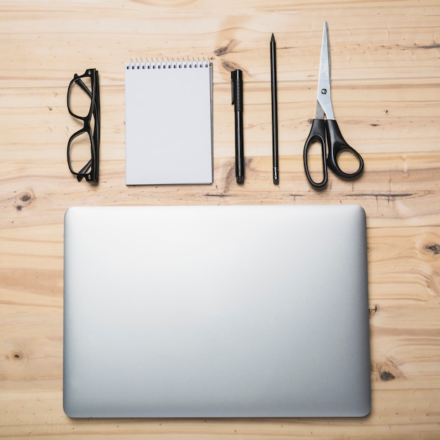 Elevated view of laptop; stationeries and spectacles on wooden background