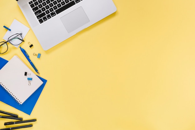 Elevated view of laptop and stationeries on yellow backdrop