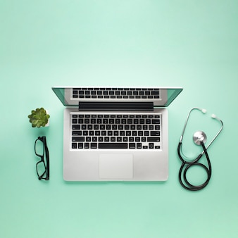 Elevated view of laptop with eyeglasses; stethoscope and succulent plant on green background