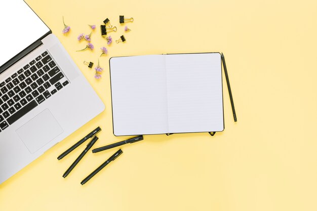 Повышенный вид ноутбука с канцелярскими принадлежностями и цветы на желтом фоне