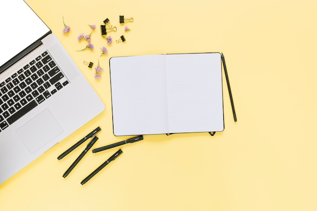 Elevated view of laptop with stationeries and flowers on yellow background