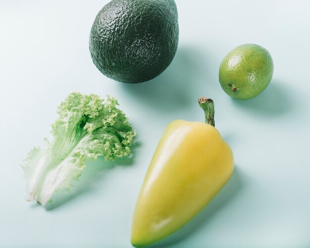 Elevated view of lettuce; lemon; avocado and bell pepper on green backdrop