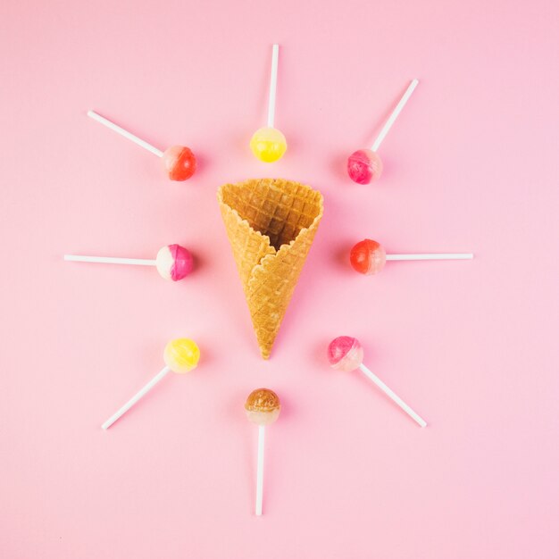 Elevated view of lollipops surrounded ice cream waffle cone on pink surface