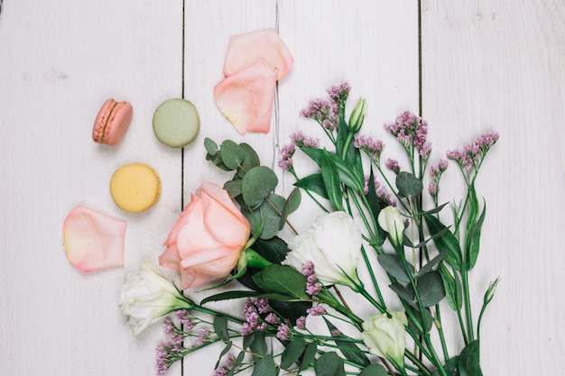 An elevated view of macaroons and fresh flower bouquet on wooden backdrop
