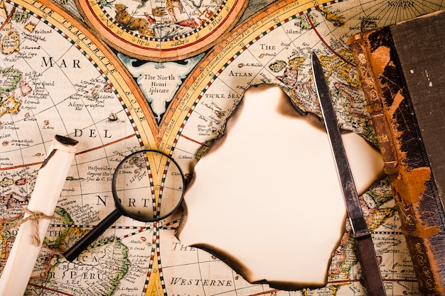 Elevated view of magnifying glass, burnt paper and knife on map
