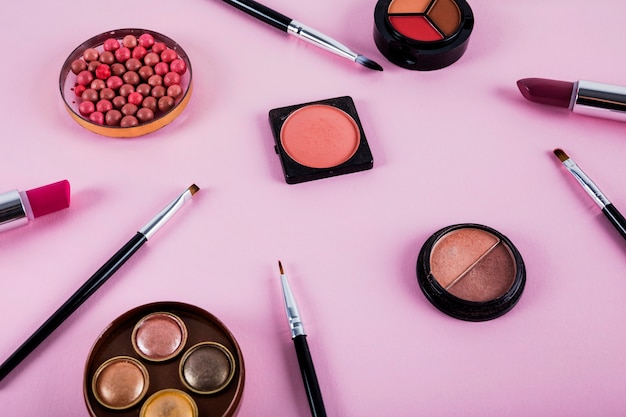 Elevated view of makeup kit with brushes on pink background