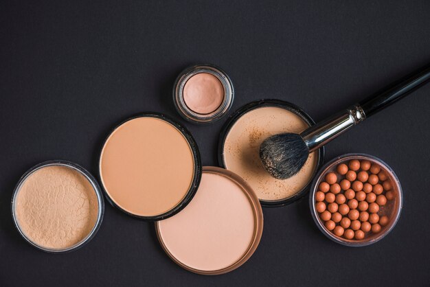 Elevated view of makeup products and brush on black surface