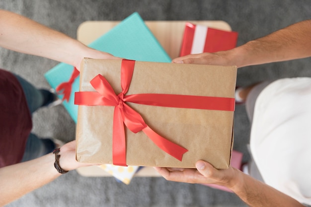 Free photo elevated view of male friend's holding wrapped gift box with red ribbon bow