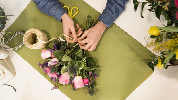 机の上の緑色の紙の上のひもで花の花束を結ぶ男性の観光客の立面図
