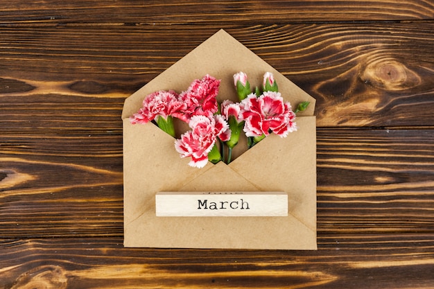 Elevated view of march text on wooden block over envelope with red flowers