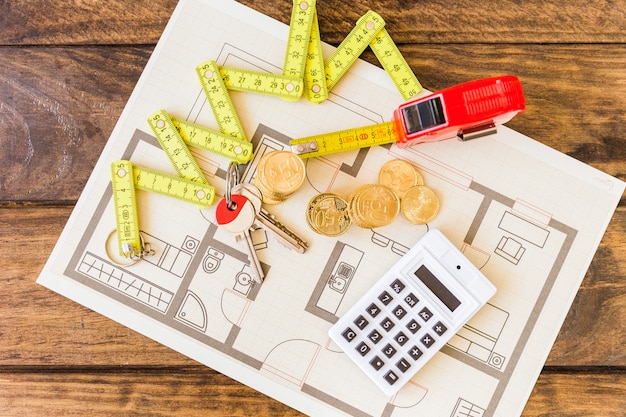 Elevated view of measure tape, stacked coins, key and calculator on blueprint