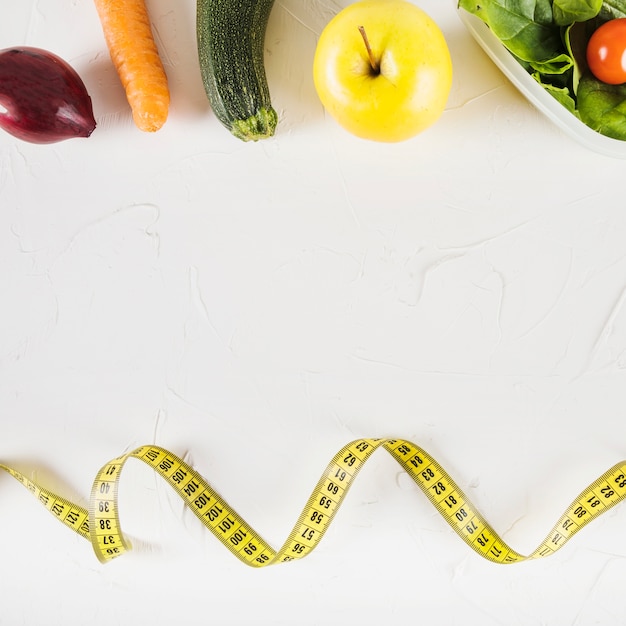 Elevated view of measuring tape and healthy food on white background