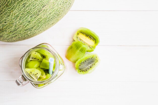 Free photo elevated view of melon fruit near kiwi slices in jar on wooden backdrop