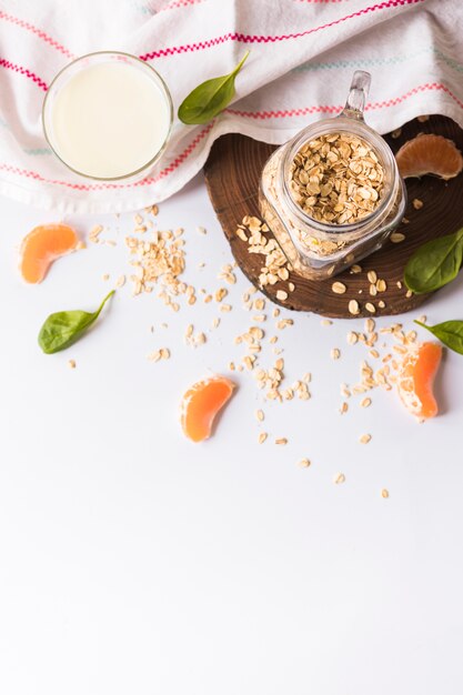 An elevated view of milk; basil leaves; oats; orange slices and napkin over white background