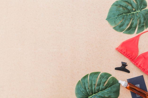 Elevated view of monstera leaf, bikini, hairclip and perfume